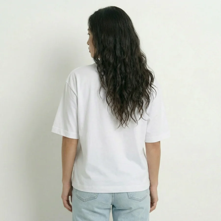Mulher de costas vestindo T-shirt Over Boxy branca e jeans claros.