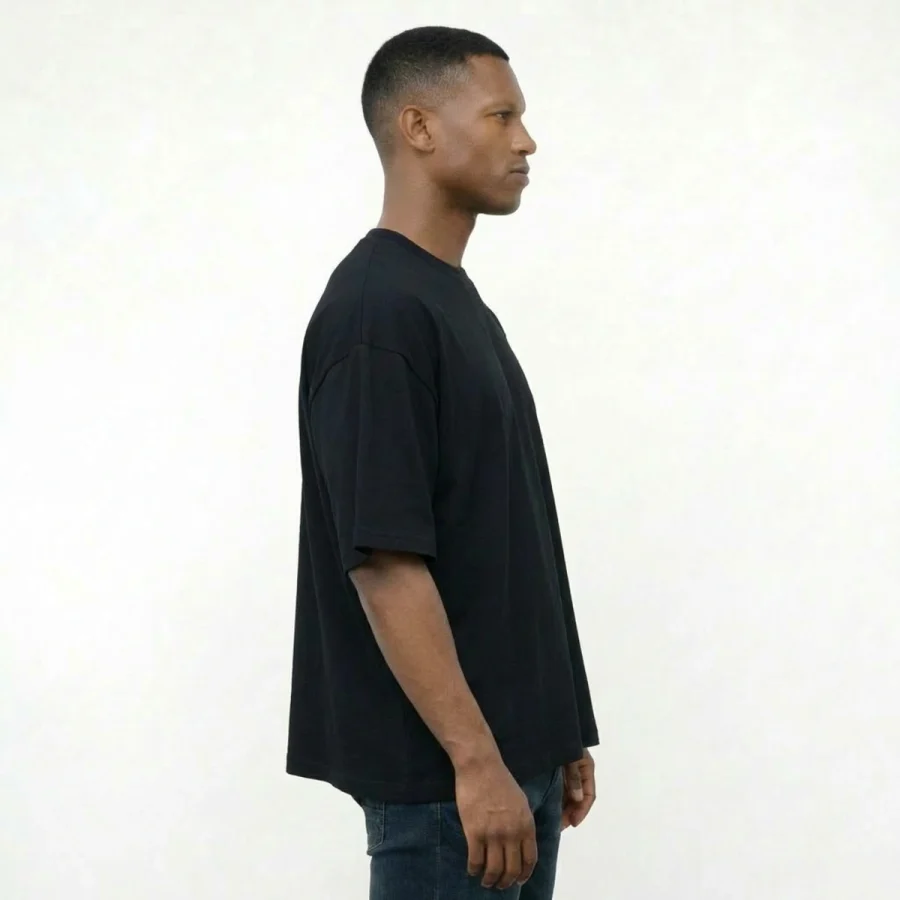 Homem de lado com T-shirt Over Boxy preto e jeans.