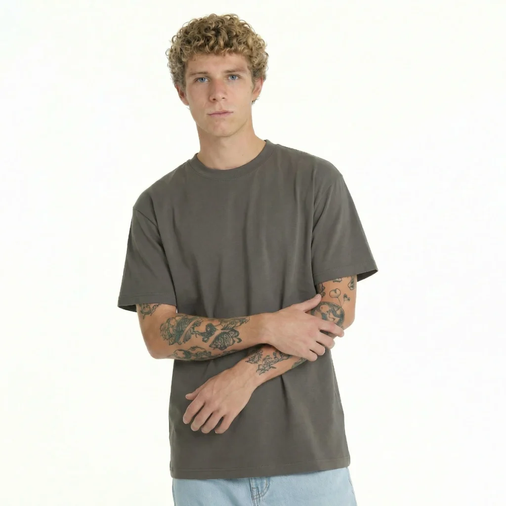Homem com T-Shirt Over Relaxed Fit castanha e braços tatuados.