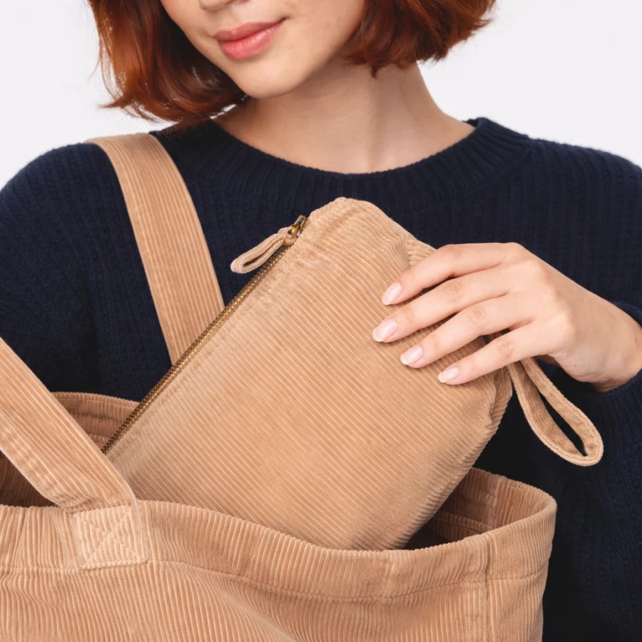 Necessaire em cor bege, com alça e zip, a ser retirada de uma bolsa.