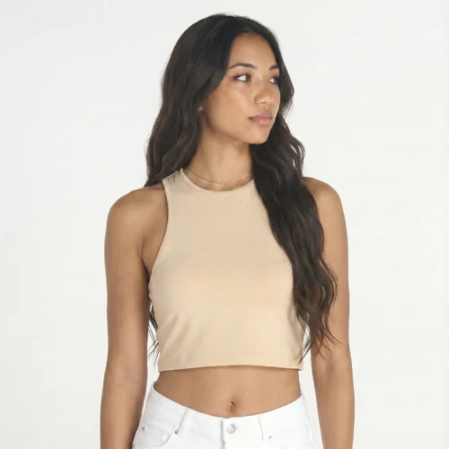 Woman with dark brown hair wearing a beige crop top and white pants.