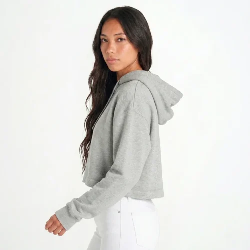 Woman with brown hair, back turned to the right and facing the camera, wearing a gray cropped hoodie and white pants.