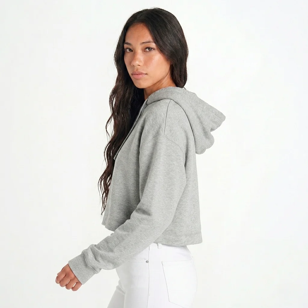 Mulher com cabelo castanho, de costas viradas para a direita e virada para a câmara, vestindo hoodie cropped cinzento e calças brancas.