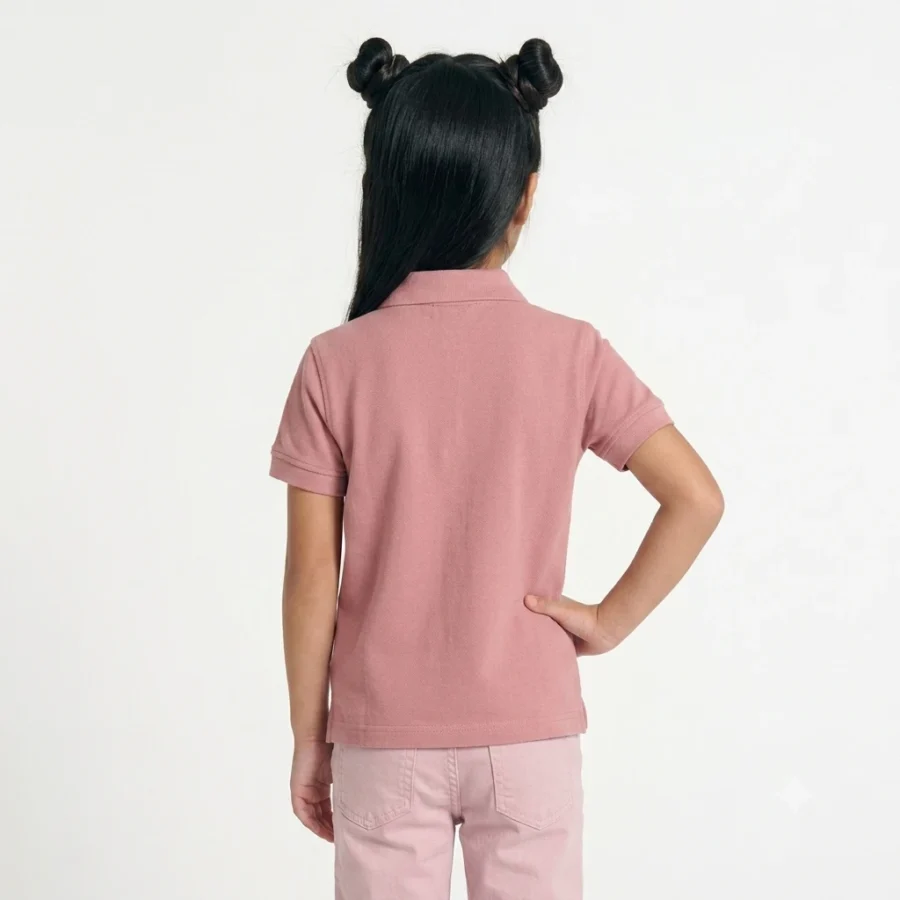 Menina com cabelo preto em dois caracóis, de costas, vestida com polo cor-de-rosa e calças claras.