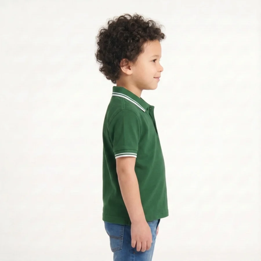 Menino com cabelo encaracolado, de perfil, vestindo polo verde e jeans.