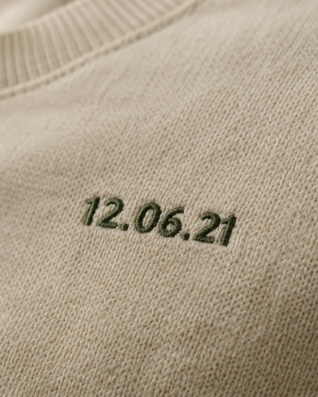 Detail of a date embroidered in green on a cream-colored sweatshirt